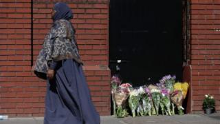 Woman passes flowers laid in Finsbury Park