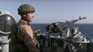 A Russian seaman stands next to a machine gun on the Russian missile cruiser Moskva (November 2015)