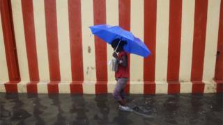 An Indian girl walks under an umbrella along a waterlogged street following heavy rain in Chennai on November 13, 2015.