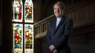 The Reverend Dr Russell Barr, the Church of Scotland's moderator designate standing in front of a stained glass window