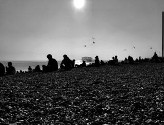 Black and white photograph of a people sat on a pebble beach