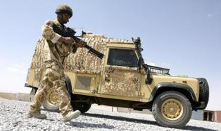 A British soldier walking beside a Snatch Land Rover in Afghanistan