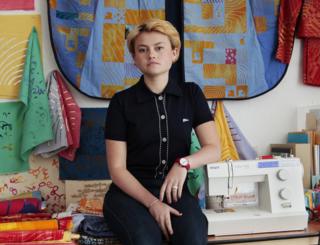 Poppy Nash sitting next to her sewing machine amongst her materials
