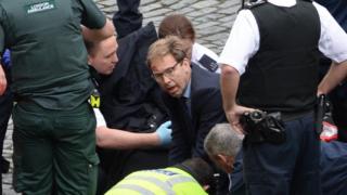 Conservative MP Tobias Ellwood helps emergency services attend to a police officer outside the Palace of Westminster