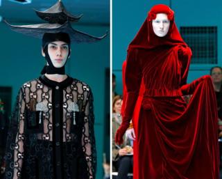Two models on the catwalk, one wearing a black top with a black hat in the shape of tiered building, the other wearing a red velvet dress including a red headscarf