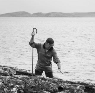 A man with a crook stands in front of the sea