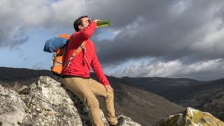 homem tomando água na garrafa em uma montanha