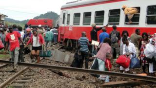A passenger escapes a train car using a window as others leave from the site of a train derailment in Eseka on October 21, 2016.