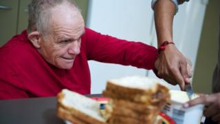 A man receiving help to spread butter on bread
