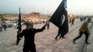 A fighter of the so-called Islamic State group holds an IS flag and a weapon on a street in the city of Mosul, 23 June 2014