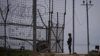A soldier stands guard at an opening to the fence of the Demilitarized Zone (DMZ) during maintenance, on Gyodong, a tiny outlying island near to the west of Seoul, on 9 May 2017