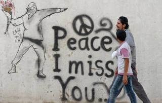 Syrian youths walk past graffiti in the rebel-held Syrian city of Minbej 10 October 2012