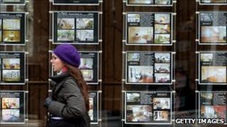 Woman walks past estate agent's window