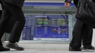 Businessmen walk past Nikkei electronic screen