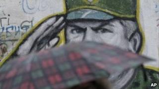 A woman with an umbrella walks past a mural of Gen Mladic in Belgrade, 26 October