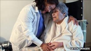 Home care worker comforting elderly woman in wheelchair