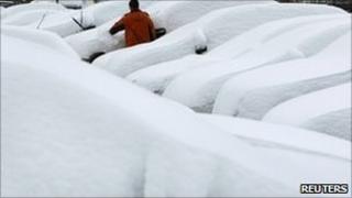 A man scrapes snow from a car in a car park at Munich airport, Germany, 2 December