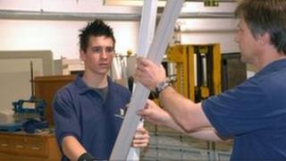 Electrician and his apprentice at work changing a strip light in a factory