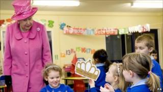 The Queen dressed in pink is shown a picture of a crown by a schoolgirl