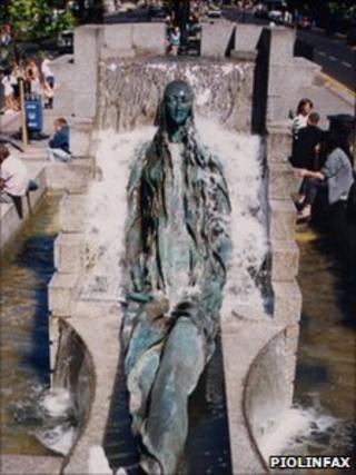 Statue of an elongated woman lying in an artificial waterfall display