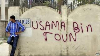 A Pakistani man leans against a wall bearing the graffiti "Osama Bin Town" near the hideout house of slain Al-Qaeda leader Osama bin Laden