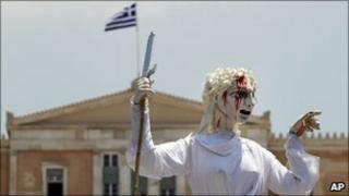 Backdropped by the Greek parliament, theatrical performers hold up a giant marionette representing Justice with a bloodied face