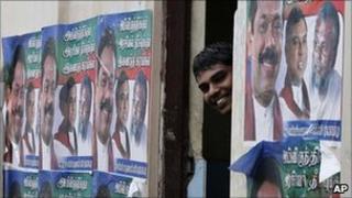 A Sri Lankan ethnic Tamil man peeps from between a wall pasted with election propaganda of Sri Lankan president Mahinda Rajapaksa"s ruling party, in Jaffna, Sri Lanka, Friday, July 22, 2011