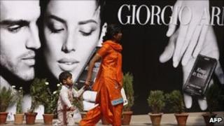 Woman and child walk past Giorgio Armani poster in India