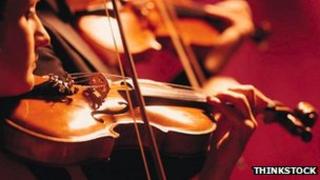 A file photo of several people playing violins against a red background