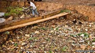 A man in Uganda's capital, Kampala, pushes his bike over a drainage channel clogged with rubbish (Photo: Edward Echwalu)