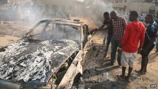Men look at the wreckage of a car following a bomb blast carried out by Boko Haram at St Theresa Catholic Church outside the Nigerian capital, Abuja, on 25 December 2011