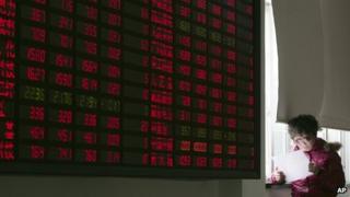 An investor looks at a document next to the stock price monitor at a private securities company Friday Jan. 20, 2012 in Shanghai, China