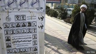A cleric walks past election posters in Tehran (27 February 2012)