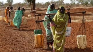 Women carry water bottles across their shoulders at a refugee camp in South Sudan