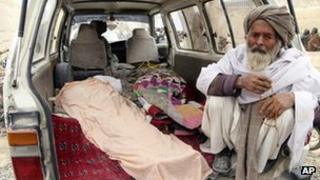 An elderly Afghan sits next to the covered body of a person allegedly killed by a US soldier in Kandahar province, 11 March.