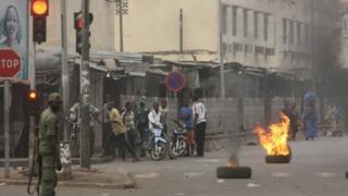 A soldier participating in a mutiny stands near civilians and burning tires lit in support of the mutiny, in Bamako, Mali Wednesday March 21 2012