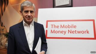 Sir Stuart Rose in front of the Mobile Money Network logo