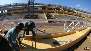 Two construction workers with the unfinished Maracana stadium behind them, 5 May 2012