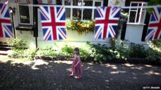 girl walks past house with union flags hanging down in front