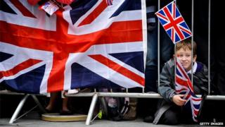 Young boy waits in the crowd with a flag prior the arrival of Queen Elizabeth II for a visit to Exeter city centre on May 02, 2012
