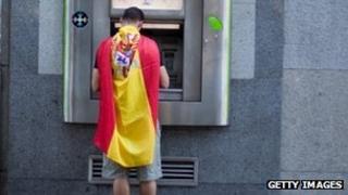 Man draped in Spanish flag withdraws cash from an ATM