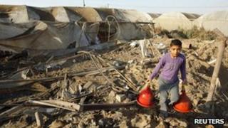 A Palestinian boy carries chicken waterers found in a coop as he walks over debris at the site of an Israeli air strike in Rafah in the southern Gaza Strip on 6 June 2012