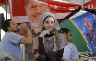 A young woman sits in front of a tent in Tahrir Square decorated with a banner showing the face of Mohammed Morsi (28 June 2012)