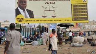 People walk past a hoarding bearing the portrait of a candidate for the Senegalese legislative elections in Dakar