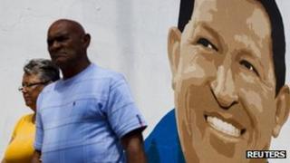 People pass a mural of incumbent Venezuelan President Hugo Chavez in Caracas, 29 June