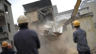 Chinese construction workers oversee a house being demolished