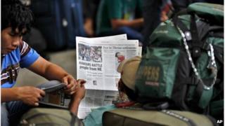 A man from India's northeastern states reads a newspaper showing news about people leaving as he waits with others to board a train home, at a railway station in Bangalore, India,Thursday, Aug. 16, 2012