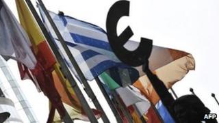 Flags outside the European Parliament next to a sculpture holding a euro sign