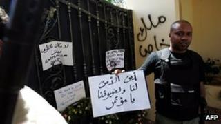 A Libyan security guard holds a slogan, which reads in Arabic "Where is the security for us and for our guests" at the main entrance of the US consulate in Benghazi on 18 September 2012