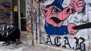 Athenians sitting in front of anti-government graffiti